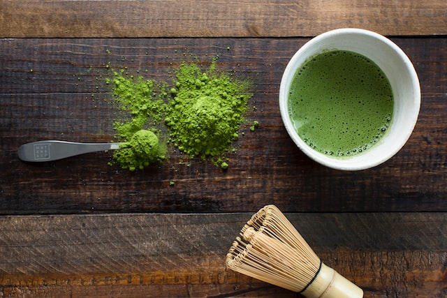 Frisch anbereiteter grüner Tee neben den dazugehörigen Utensilien sowie Teepulver.