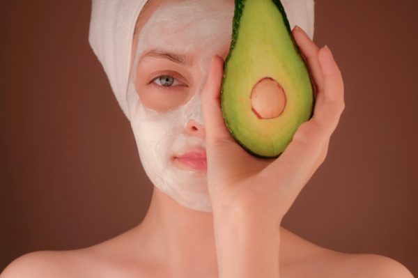 Eine Frau mit einer Maske im Gesicht hält sich eine Avocado vors Gesicht