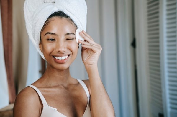 Eine Frau, die die Haare in ein Handtuch gewickelt hat, wischt sich mit einem Reinigungspad über das Gesicht
