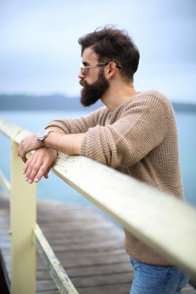 Ein Mann mit Bart steht an Brüstung, im Hintergrund siehst du Meer