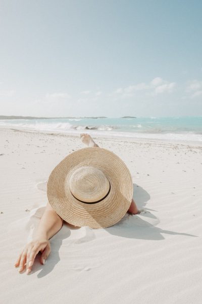 Eine Person liegt mit großem Sonnenhut am Strand
