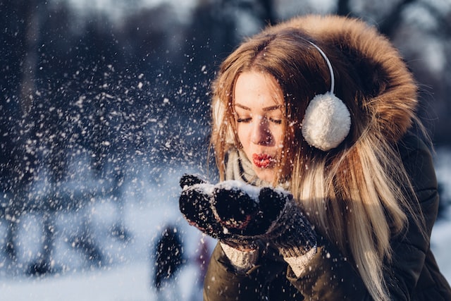 Frau mit Ohrenschützern, die in Schnee pustet