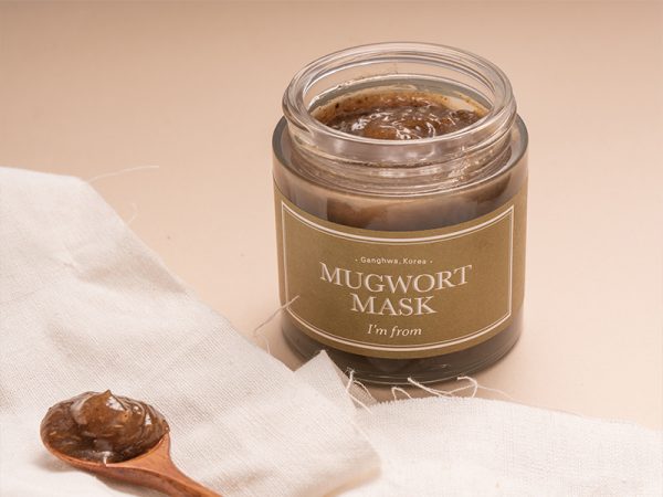 Ein offener Topf voller Creme-Maske daneben ein Holzlöffel voller Produkt