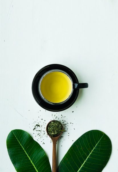 Teeblätter, Löffel und eine Tasse grüner Tee