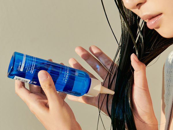 Eine Frau mit langen, schwarzen, nassen Haaren verteilt darin ein Pflegeprodukt von Lador aus einer blauen Flasche