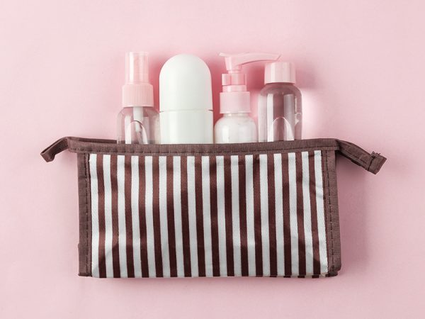 Eine gestreifte Kosmetiktasche aus der kleine Fläschchen mit rosa Deckeln herausschauen 