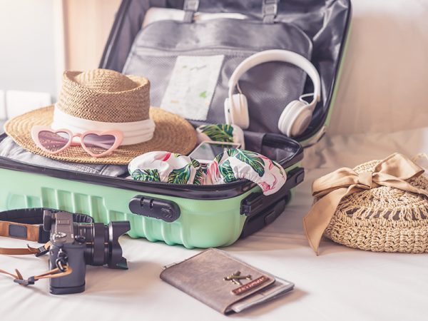 Ein offener, gepackter Koffer mit Kamera, Hut, Kopfhörern, Kleidung und vielen weiteren Gegenständen
