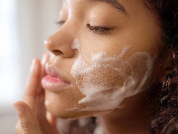 Eine Frau wäscht sich das Gesicht mit einem sanften Schaum. Ihre Augen sind geschlossen